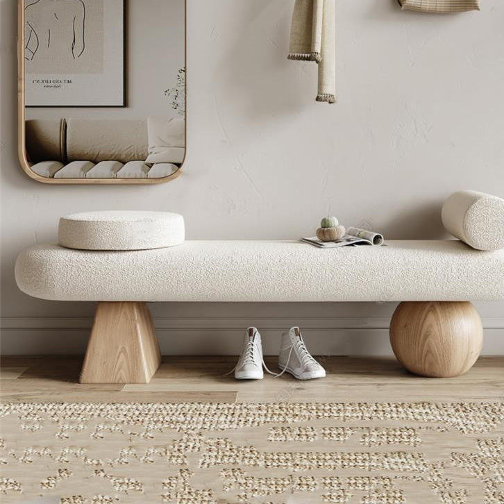 75-inch off-white boucle upholstered bench with sculptural natural wood legs (triangular block and round sphere), styled with a round bolster and seat pad, small decor on top and sneakers placed underneath.