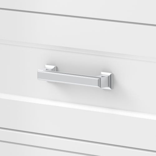 Close-up of a chrome rectangular drawer pull mounted on a white painted wood vanity drawer front with subtle horizontal shaker grooves, a contemporary glam hardware detail.