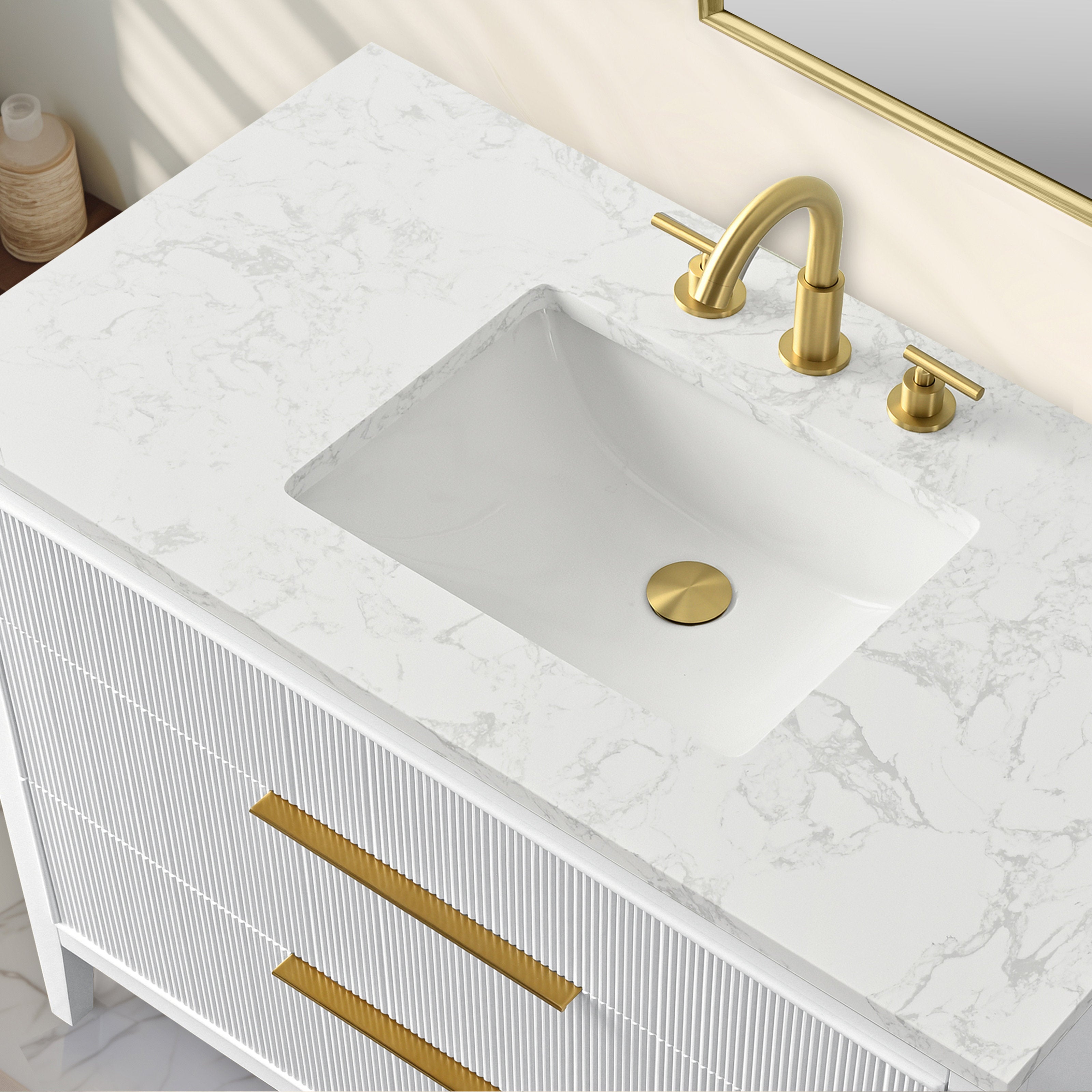 Overhead view of a single-sink bathroom vanity featuring a white marbled stone top, rectangular white ceramic sink, fluted solid wood white cabinet and matte gold faucet, drain cover and long gold drawer pulls.