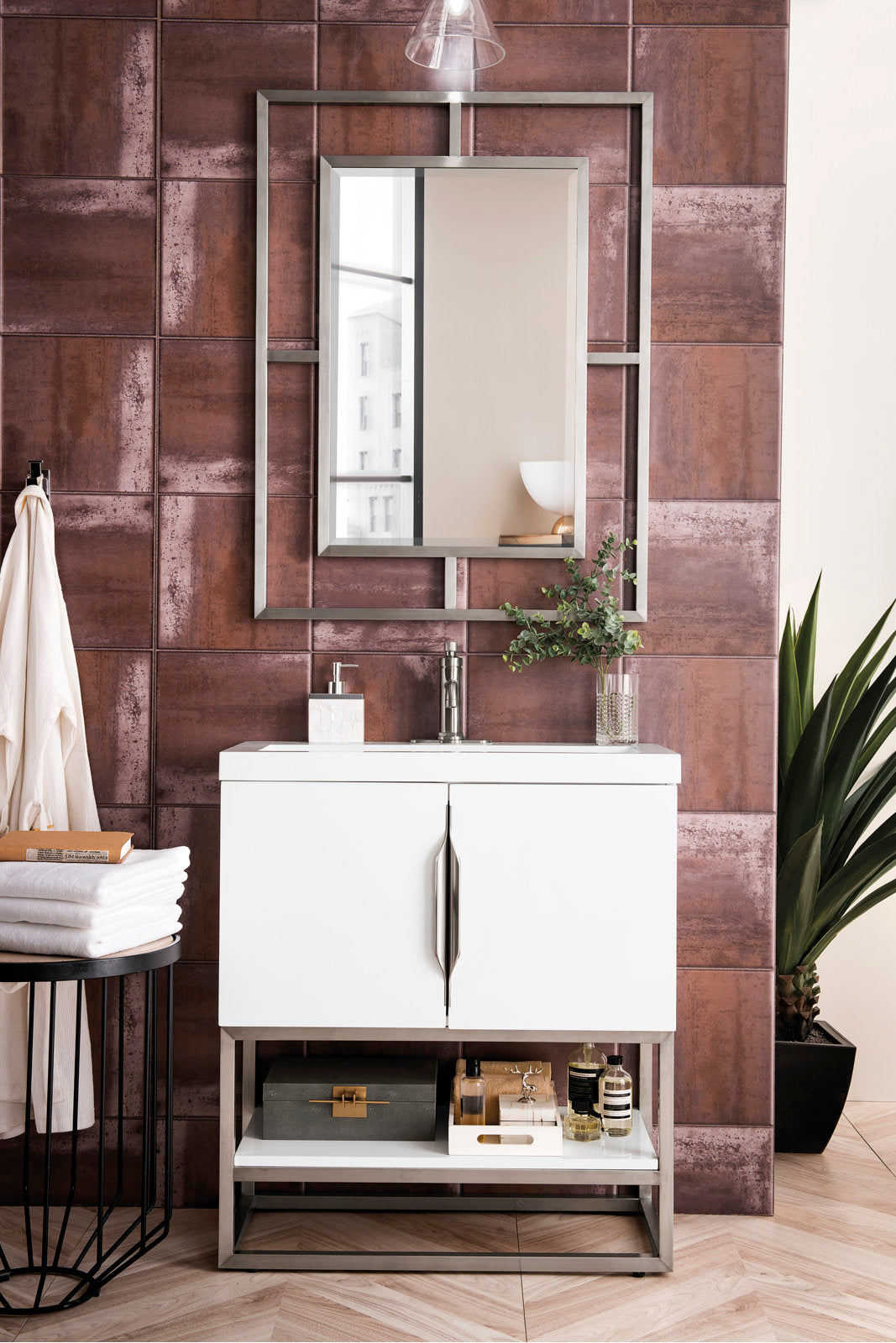 Contemporary white 31.5-inch single-sink solid wood bathroom vanity with stone countertop and integrated ceramic basin, stainless-steel legs and handles, rectangular framed mirror against textured brown tile wall with plant and towels.