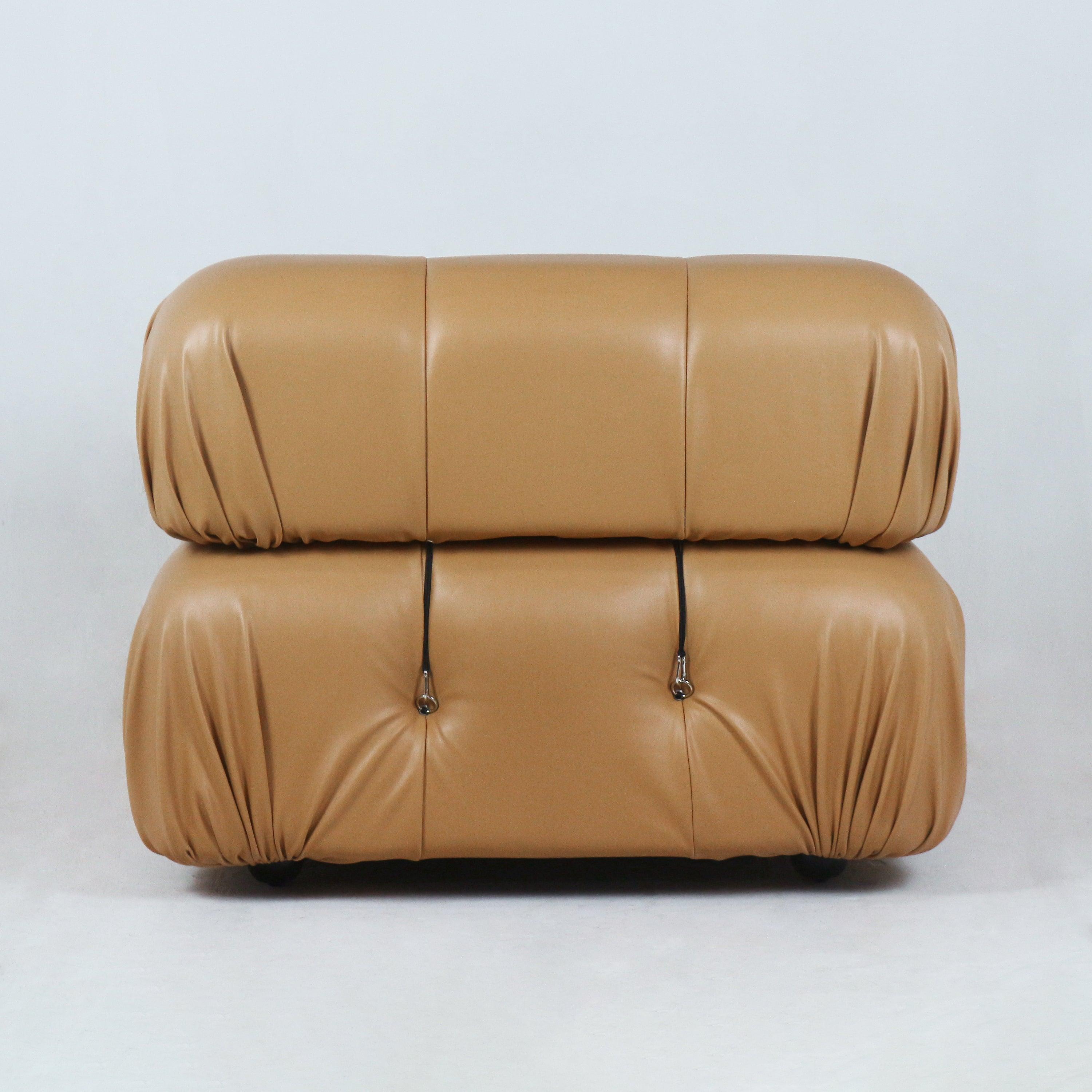 Front view of a tan leather modern sofa with two stacked rounded cushions, gathered corner pleats, tufted buttons with metal strap hardware and a low profile on short feet.