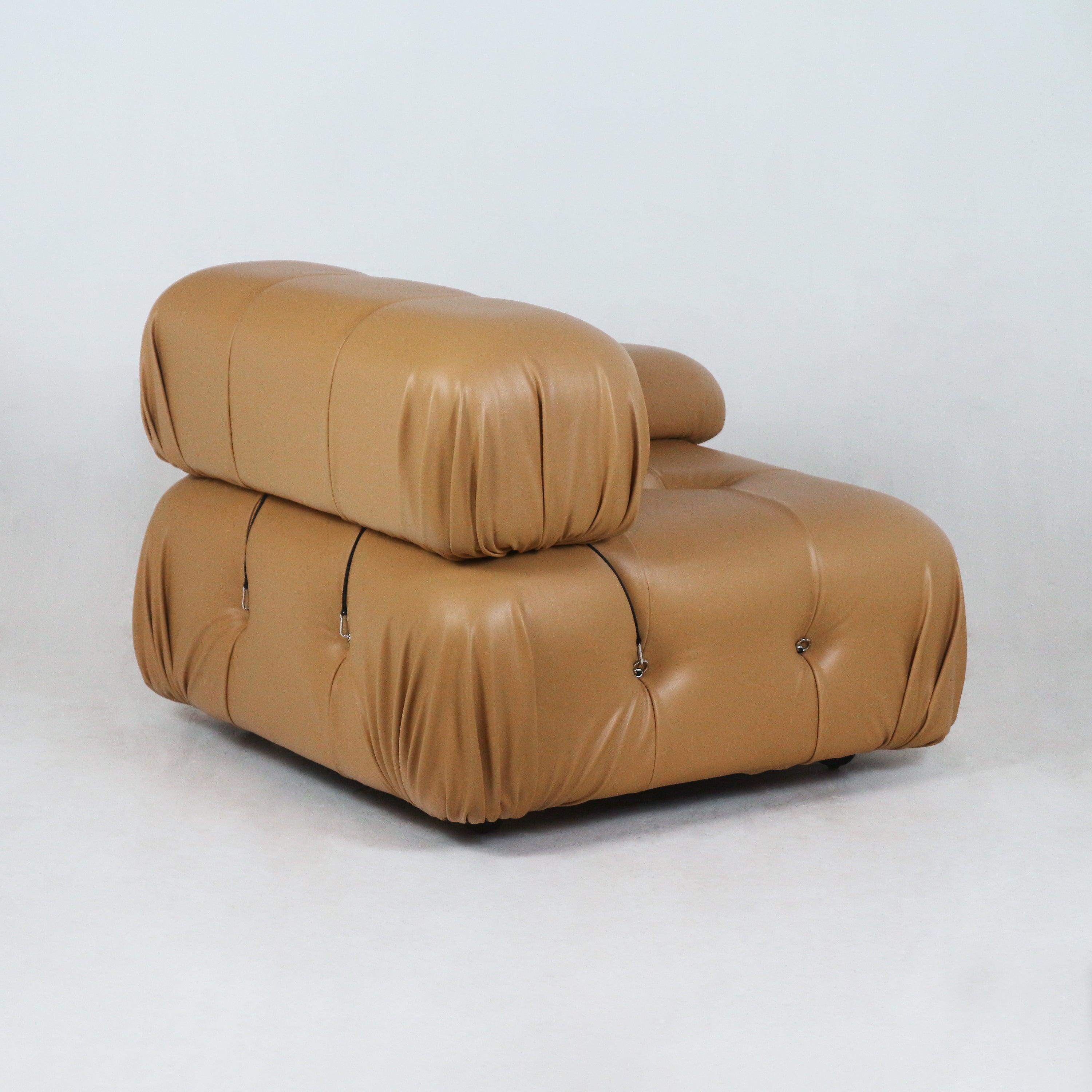 Low-profile modern tan leather sofa module with overstuffed rounded cushions, tufted detailing and visible black cord-and-metal loop fasteners, shown on a plain white studio background.