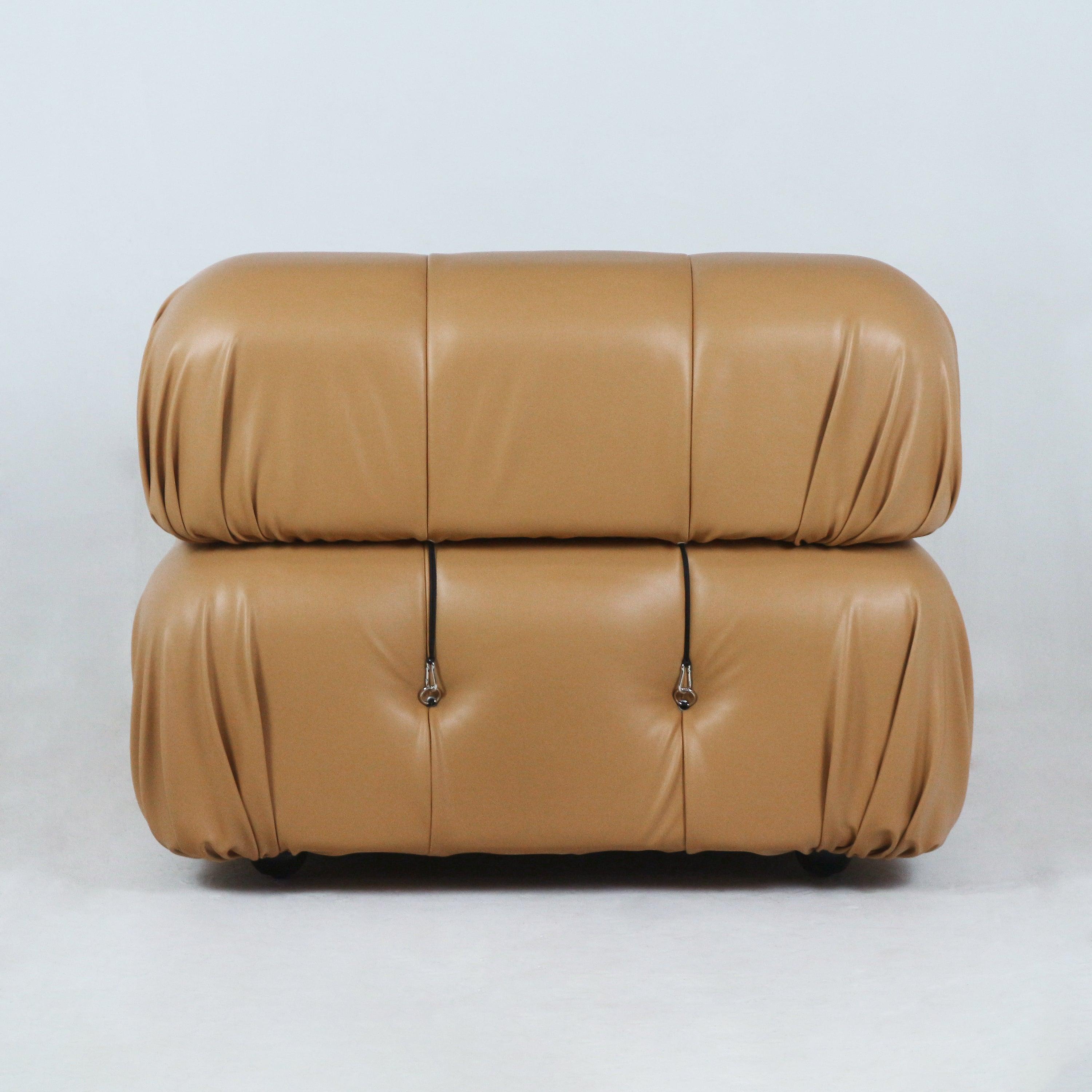 Front view of a modern tan leather sofa with two stacked rounded cushions, subtle tufting and black strap hardware on a white backdrop.