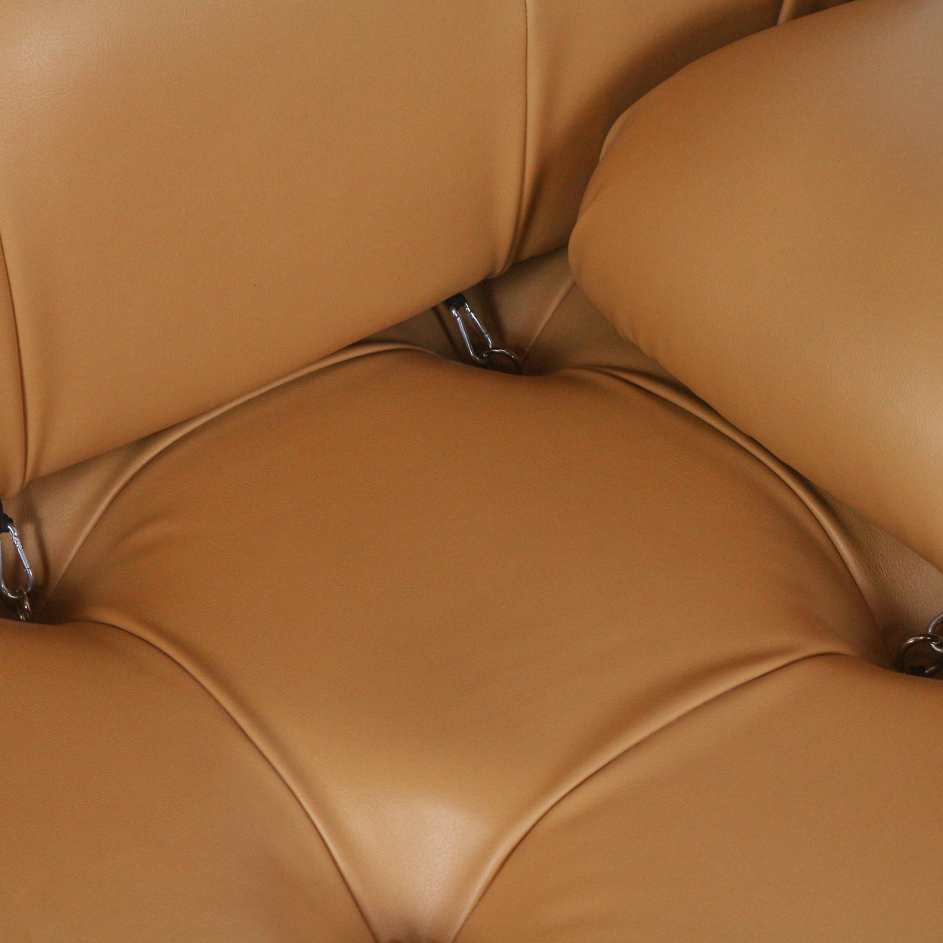 Close-up of a tan leather modern sofa showing tufted rounded seat and back cushions with stitched seams and visible chrome attachment rings.
