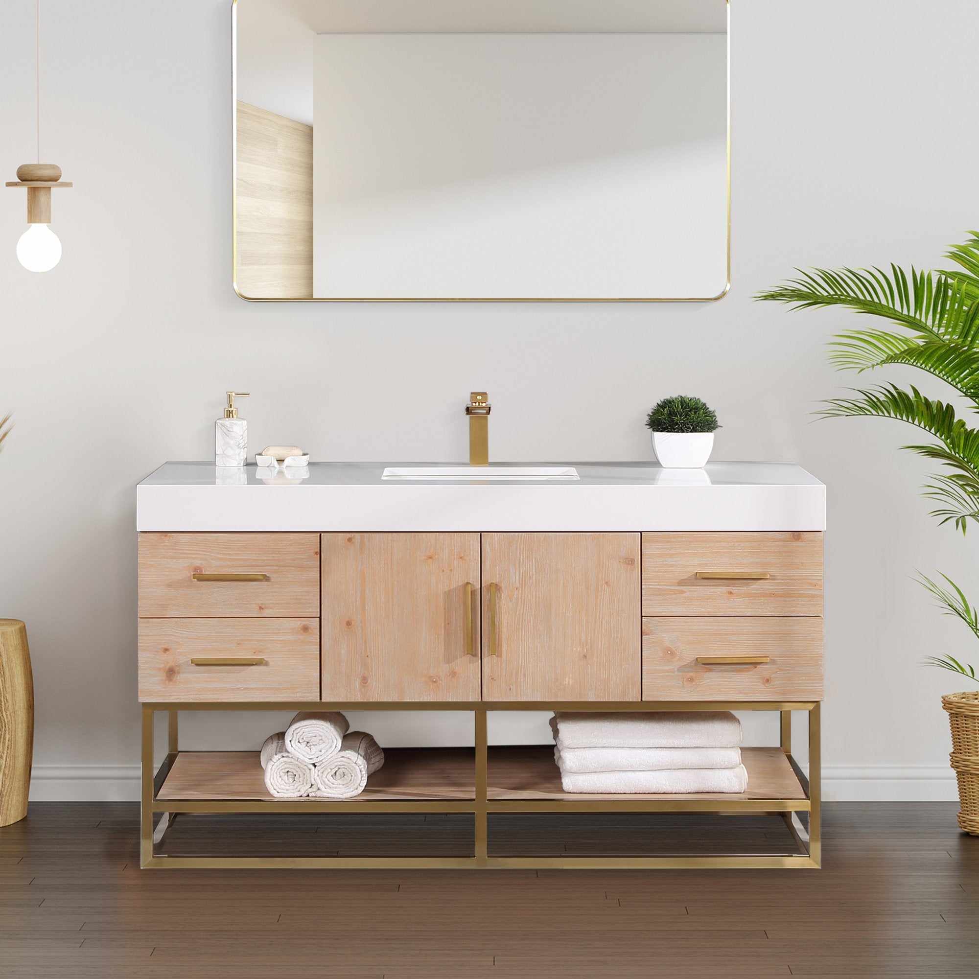 Modern 60-inch light natural wood bathroom vanity with white composite stone top, rectangular undermount sink, brass-finish faucet and handles, open lower shelf with rolled towels, gold-framed mirror and potted plant.