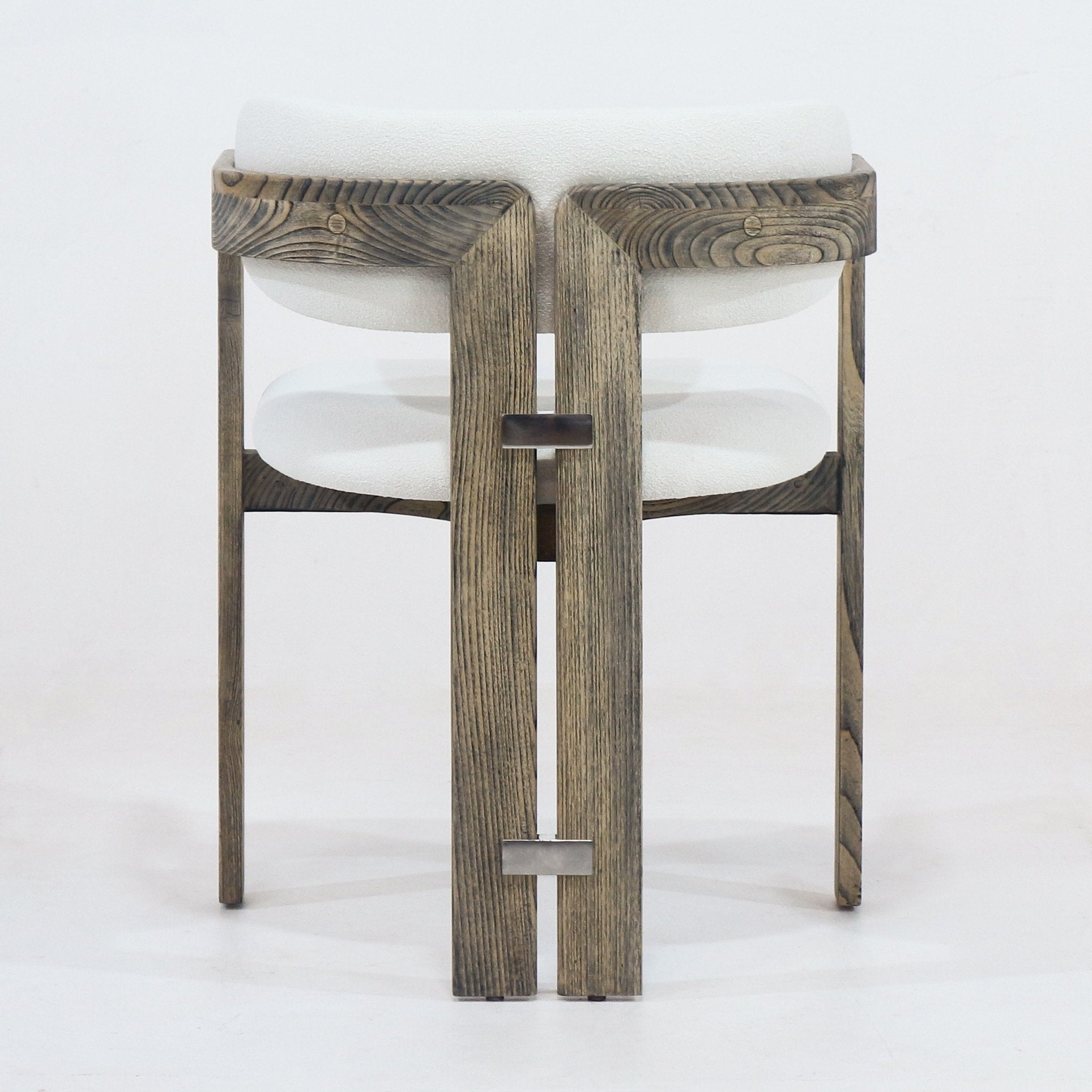 Rear view of a rustic brown stained wood dining chair with cream boucle upholstered cushioned seat and back, integrated curved arms and two small metal rectangular connectors on the vertical rear slats.