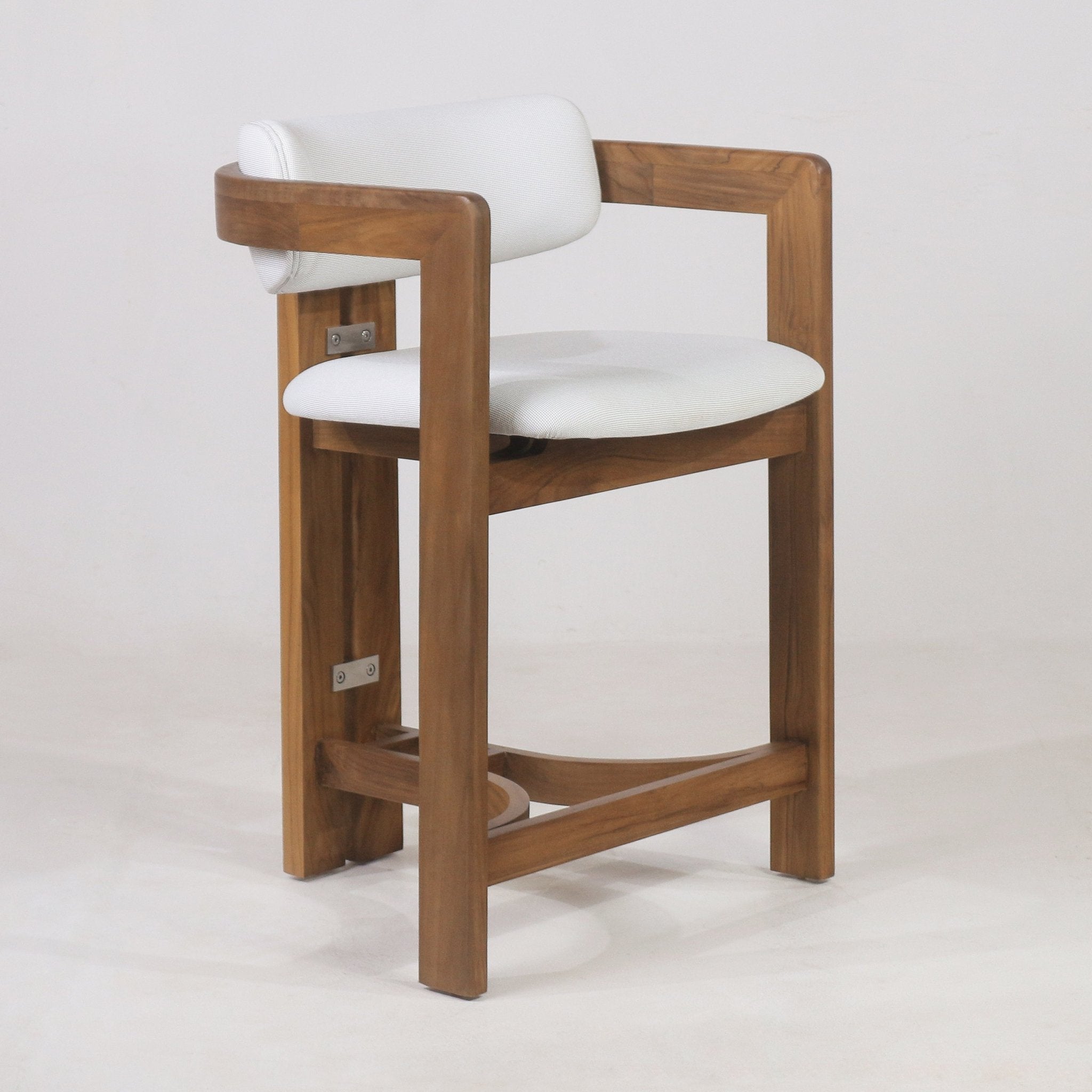Teak outdoor bar stool with white fabric upholstered round seat and cylindrical cushioned back embraced by a curved teak arm frame, solid teak legs and integrated curved footrest in a coastal-contemporary style.