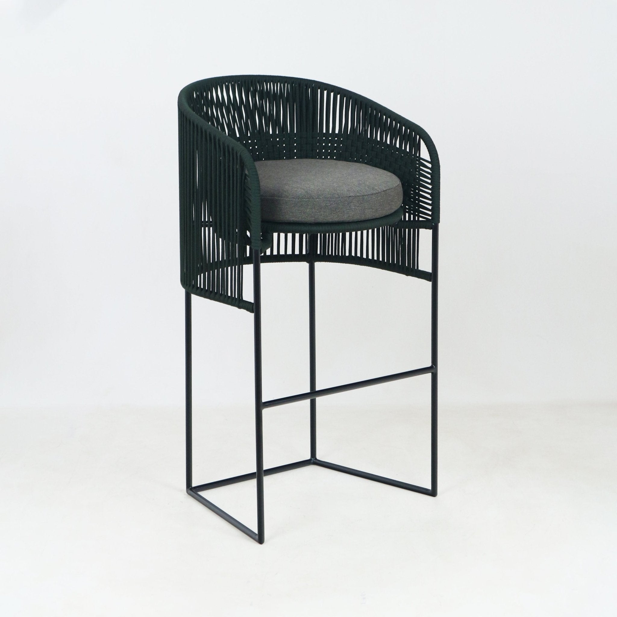 Coastal-style outdoor bar stool with dark green woven rope back and arms, round gray fabric cushion, and slim black metal sled base with footrest, shown on a plain light background.