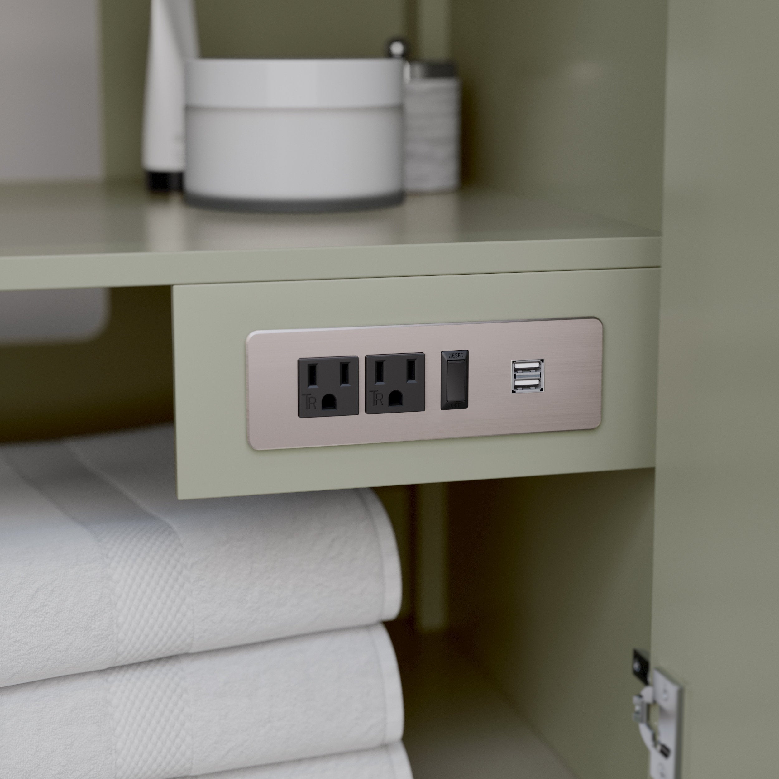 Close-up inside a stone-colored modern solid wood vanity showing a brushed metal outlet plate mounted beneath a shelf with two electrical receptacles, a reset switch and dual USB ports; folded white towels below.