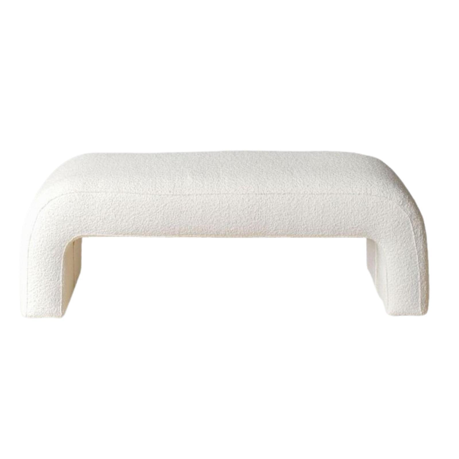 White boucle-upholstered end-of-bed bench with a low, armless silhouette, rounded corners and open U-shaped legs, shown against a white background.