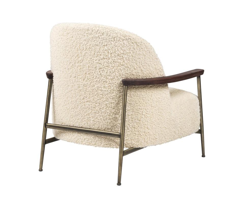 Three-quarter rear view of a cream boucle accent chair with a rounded upholstered back, dark wood armrests and slender antique-brass metal frame and legs in a modern contemporary silhouette.