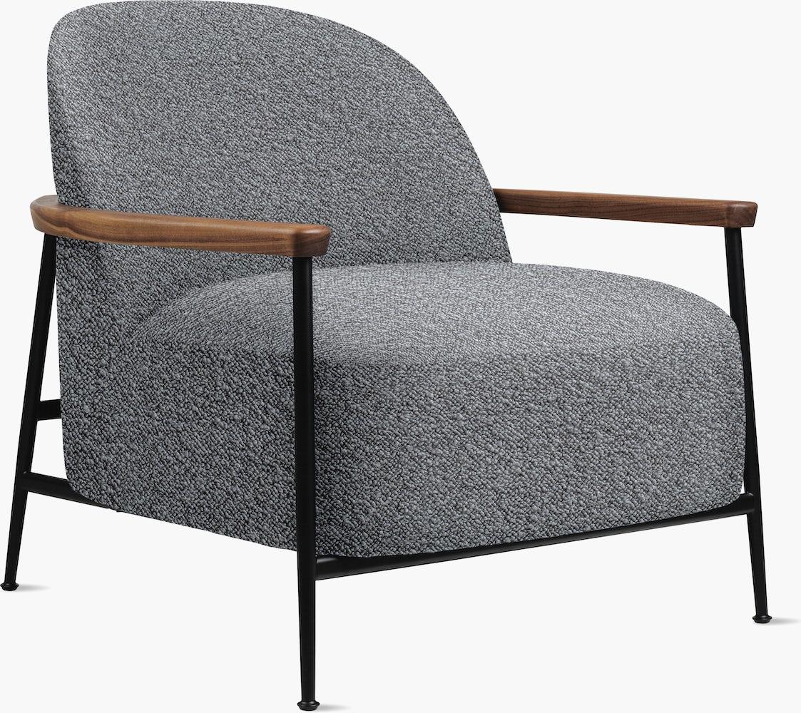 Contemporary accent chair upholstered in gray boucle fabric with a rounded back, thick cushioned seat, walnut-finished wooden armrests and slim black metal legs and frame.