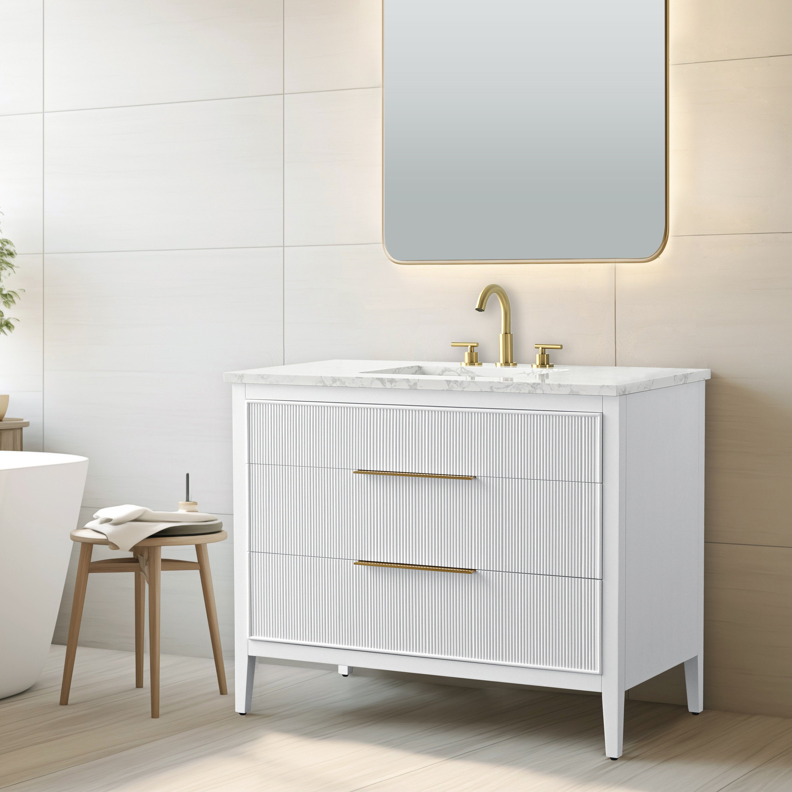 Freestanding modern solid wood bathroom vanity with stone marble top, white fluted drawer fronts, two long gold handles and matching gold faucet, shown beneath a backlit rounded mirror with a wooden stool nearby.