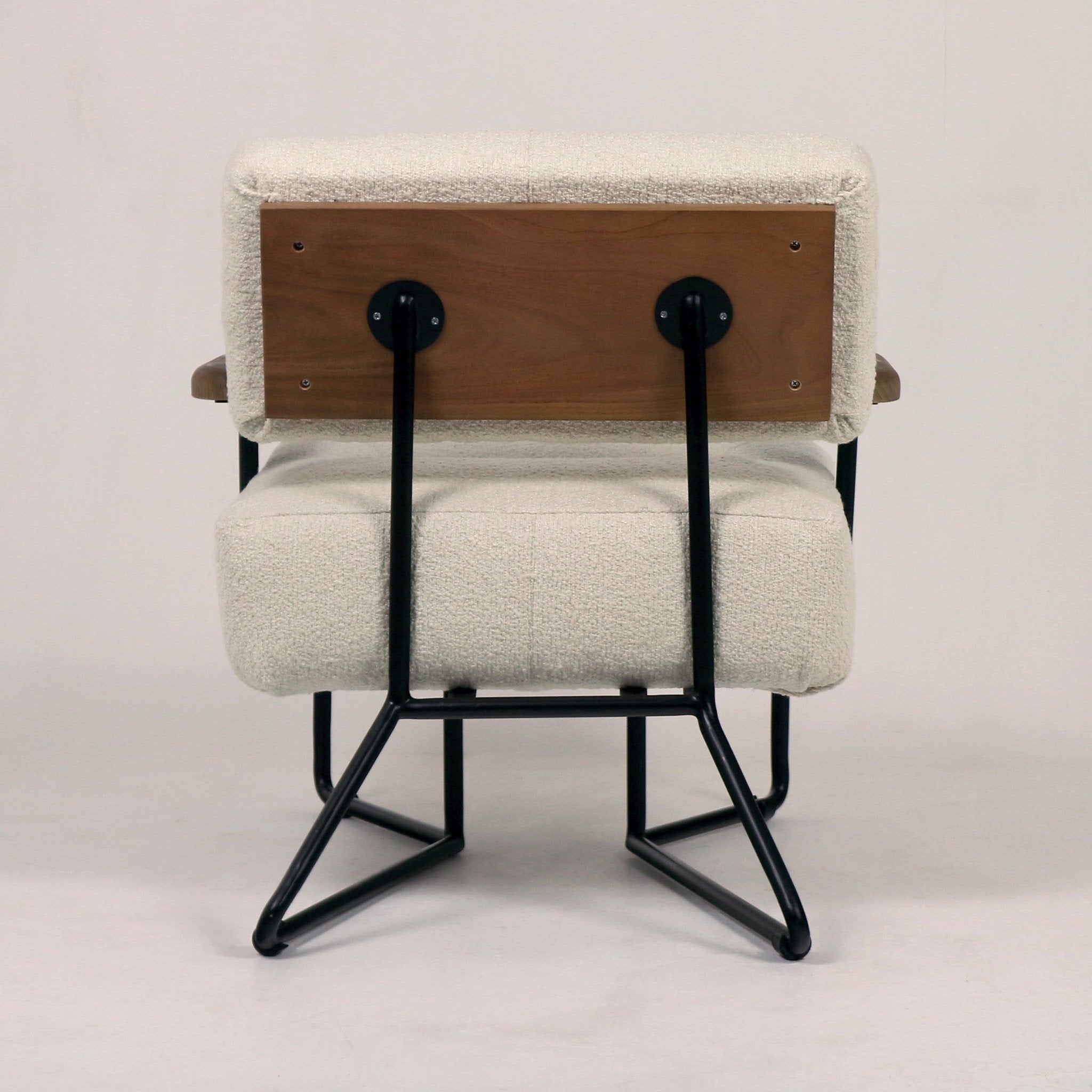 Rear view of a modern lounge chair upholstered in beige boucle fabric with a walnut-tone wooden back panel and black metal tubular frame and sled-style legs.