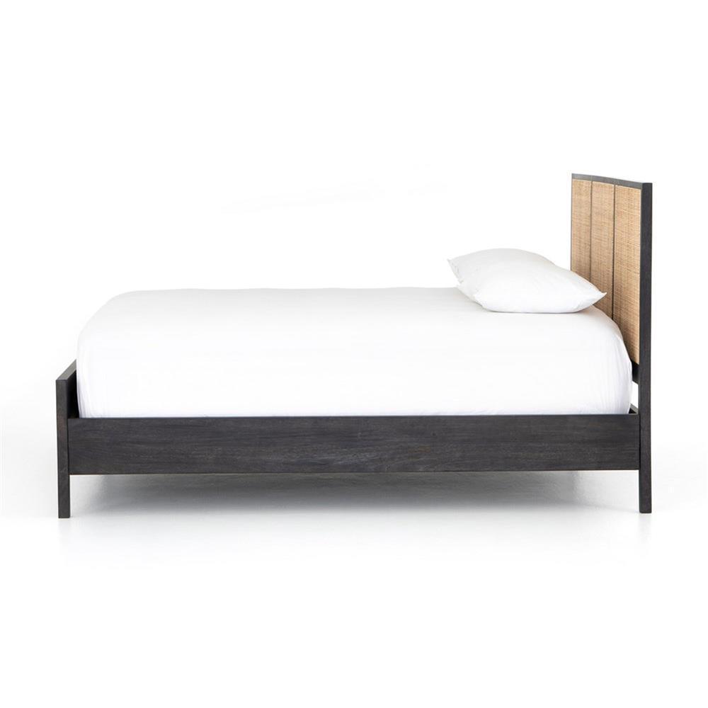 Side view of a teak platform bed with a dark stained solid wood frame and woven natural rattan cane headboard, shown with white bedding and a pillow on a plain white background.