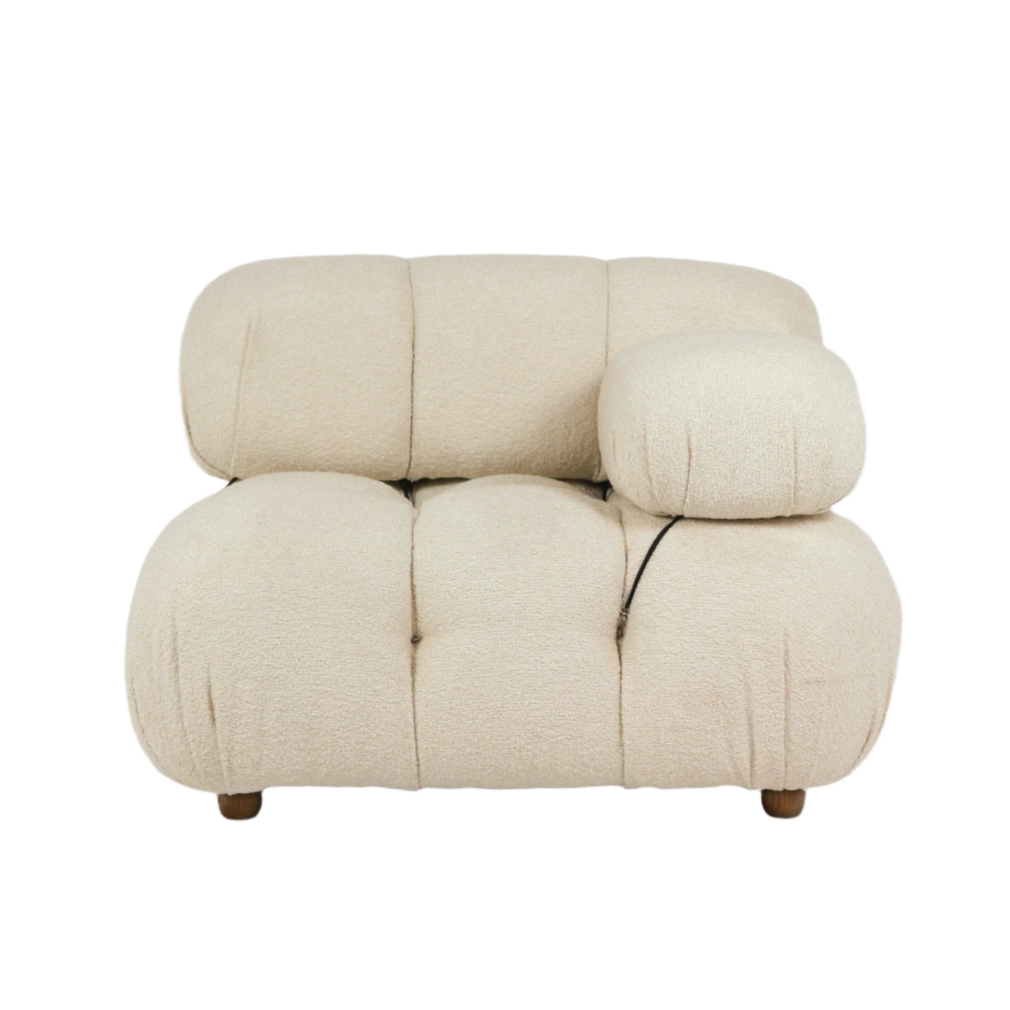 Low-profile modern sofa upholstered in cream boucle fabric with plush rounded tufted cushions, short wooden legs and a removable bolster pillow secured by black cord straps.