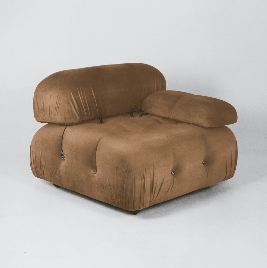 Oversized tan leather modern lounge chair with rounded tufted cushions, a single low arm pillow, visible soft wrinkles and metal loop fasteners, photographed on a neutral studio background.