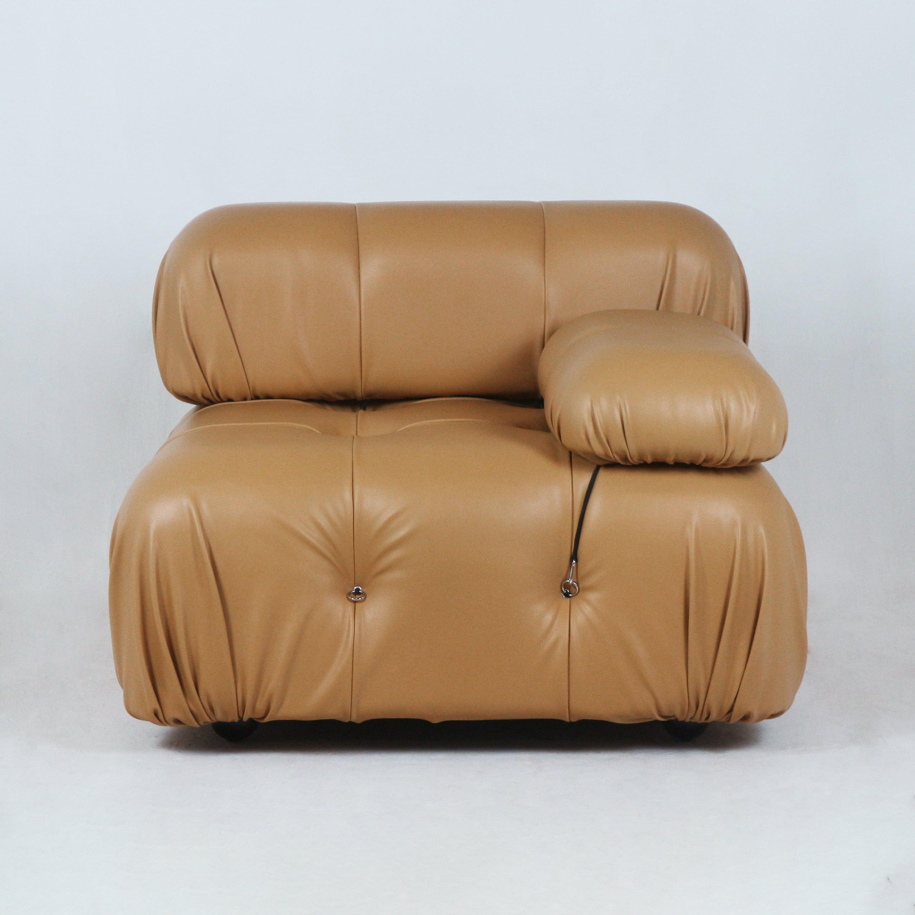 Front view of a tan leather modern lounge chair with rounded, plush tufted cushions, low profile seat and a single padded armrest accented by metal ring hardware and a black cord detail.
