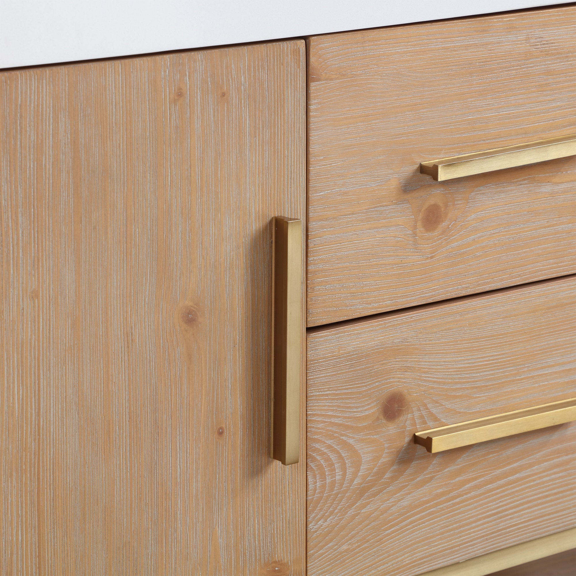 Close-up of a light brown natural wood bathroom vanity door and drawers with a white composite stone countertop edge and brushed brass bar handles, highlighting wood grain texture and panel seams.
