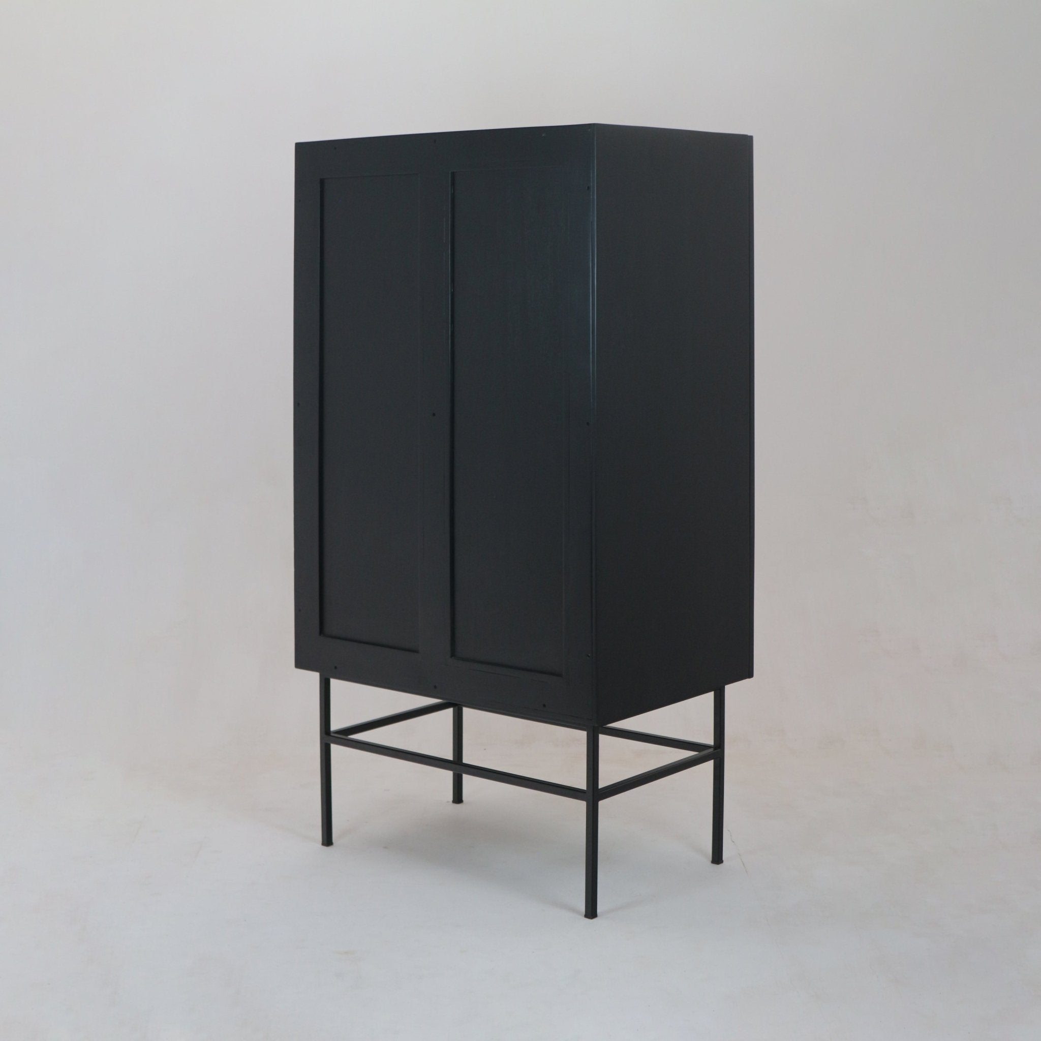 Tall black solid wood wardrobe with two paneled doors elevated on a slim black steel frame base, finished in a modern minimalist style and photographed against a neutral studio background.