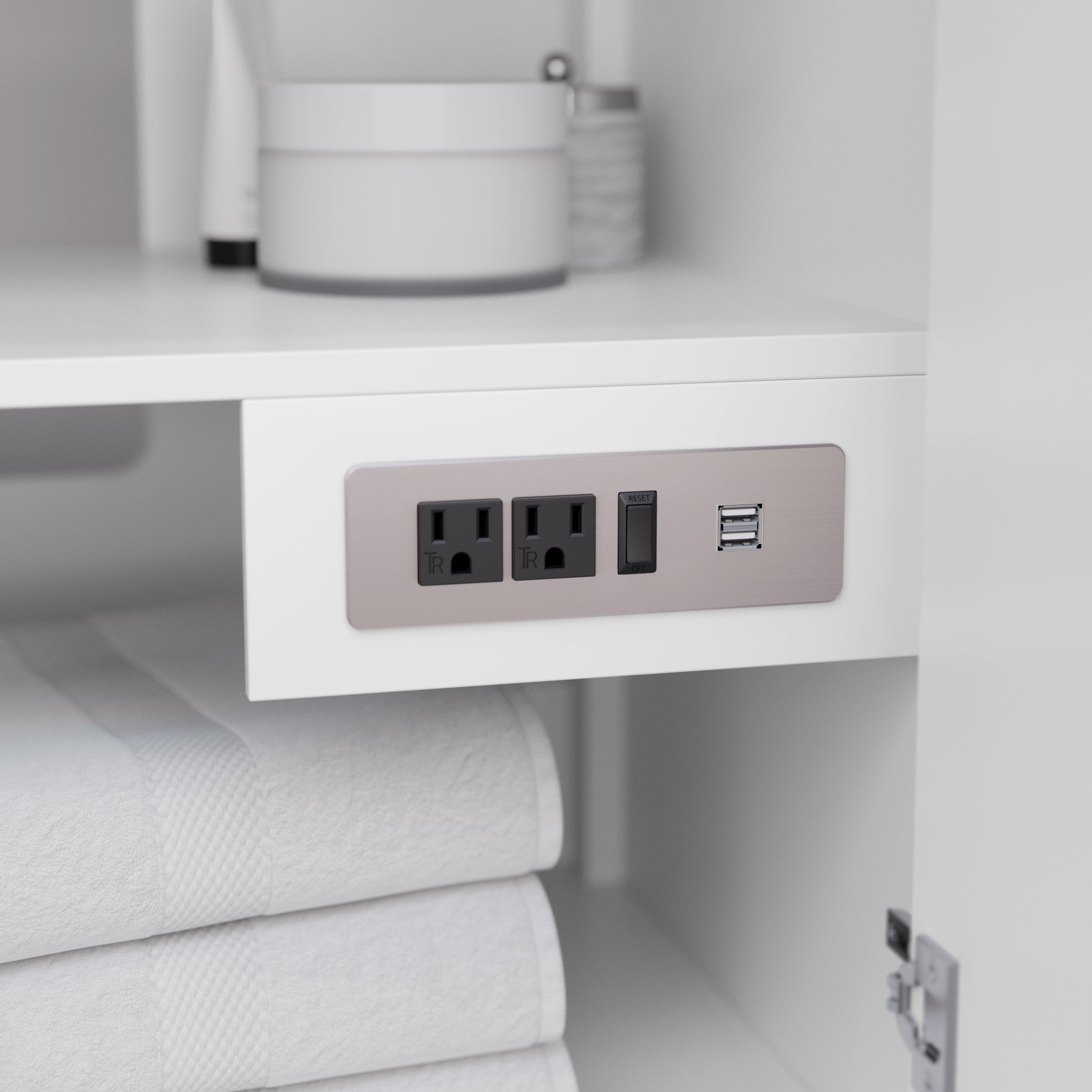 Close-up of a white wood vanity interior showing a brushed-nickel power plate with two grounded outlets, a GFCI reset switch and dual USB ports above neatly folded white towels.